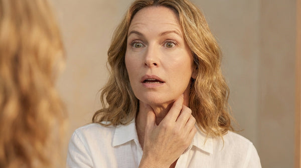 Middle-aged woman examining jawline in mirror with hand on chin, skincare concern